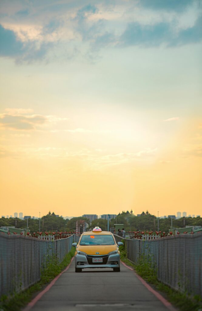 A solitary taxi drives down a narrow road against a stunning evening sky.