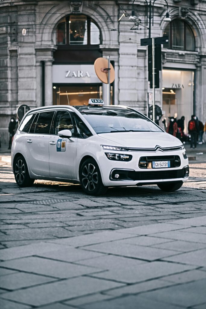 A modern white taxi car driving on a stylish city street with architectural backdrop.